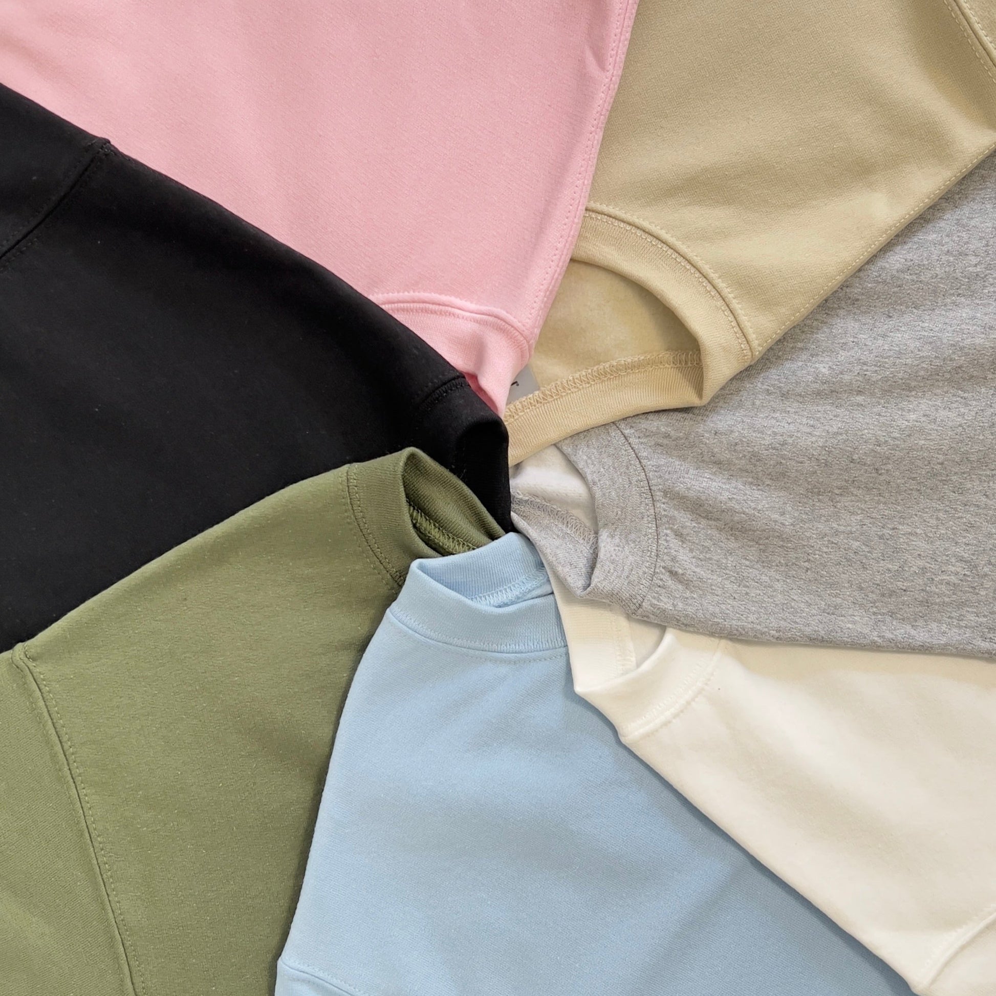 Different color options of sweatshirts are shown: pink, beige/sand, gray, white, blue, green, and black.